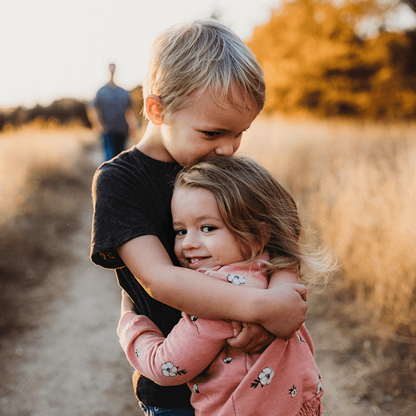 Siblings hugging in sunset expertly lit, framed, and composed.